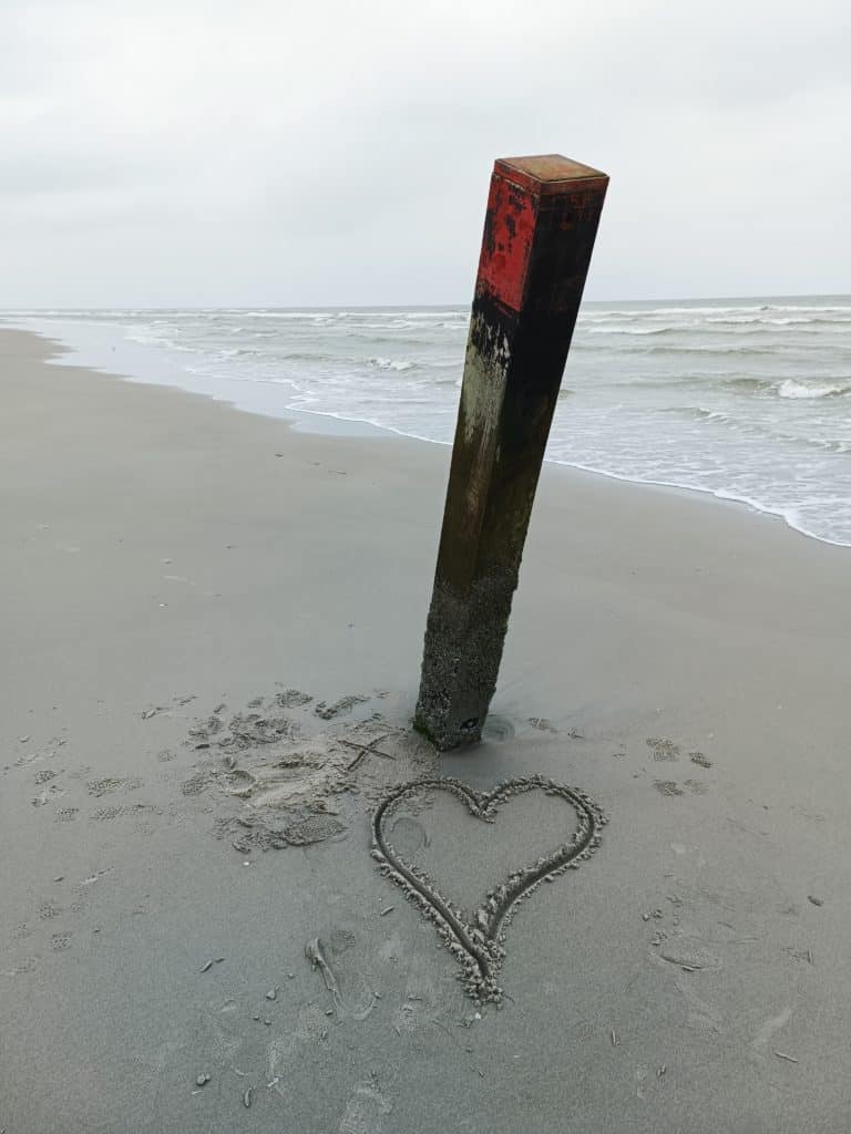 Strandpaal met een hartje in het zand